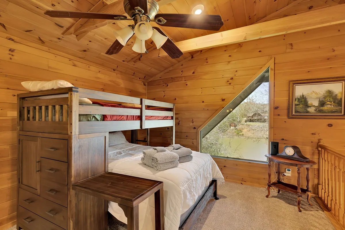 A comfortable lower-level bunk room with a bunk bed, large window, wooden furniture, and a decorative painting, creating a warm, kid-friendly space for rest and play.