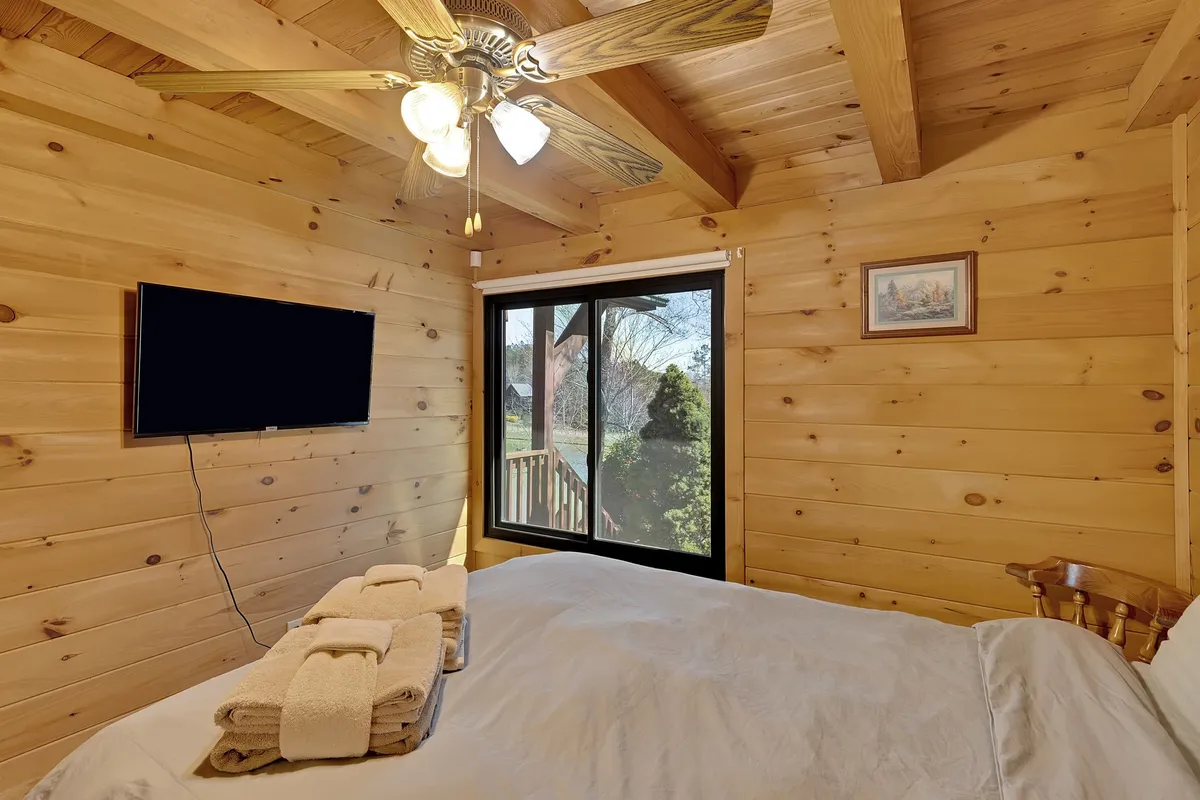 A loft-style bedroom with a wooden ceiling, large window letting in sunlight, and a comfortable bed with towels, inviting guests to unwind while enjoying views and tranquility.