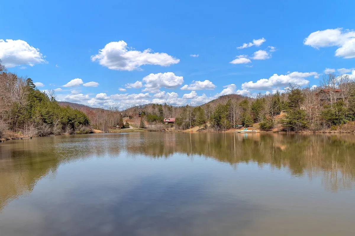 A tranquil view over Laurel Lake, with calm waters reflecting the surrounding trees and distant hills. Subtle cloud formations add depth to the serene landscape. This wide, open perspective hints at opportunities for fishing, canoeing, wildlife watching, and stargazing.