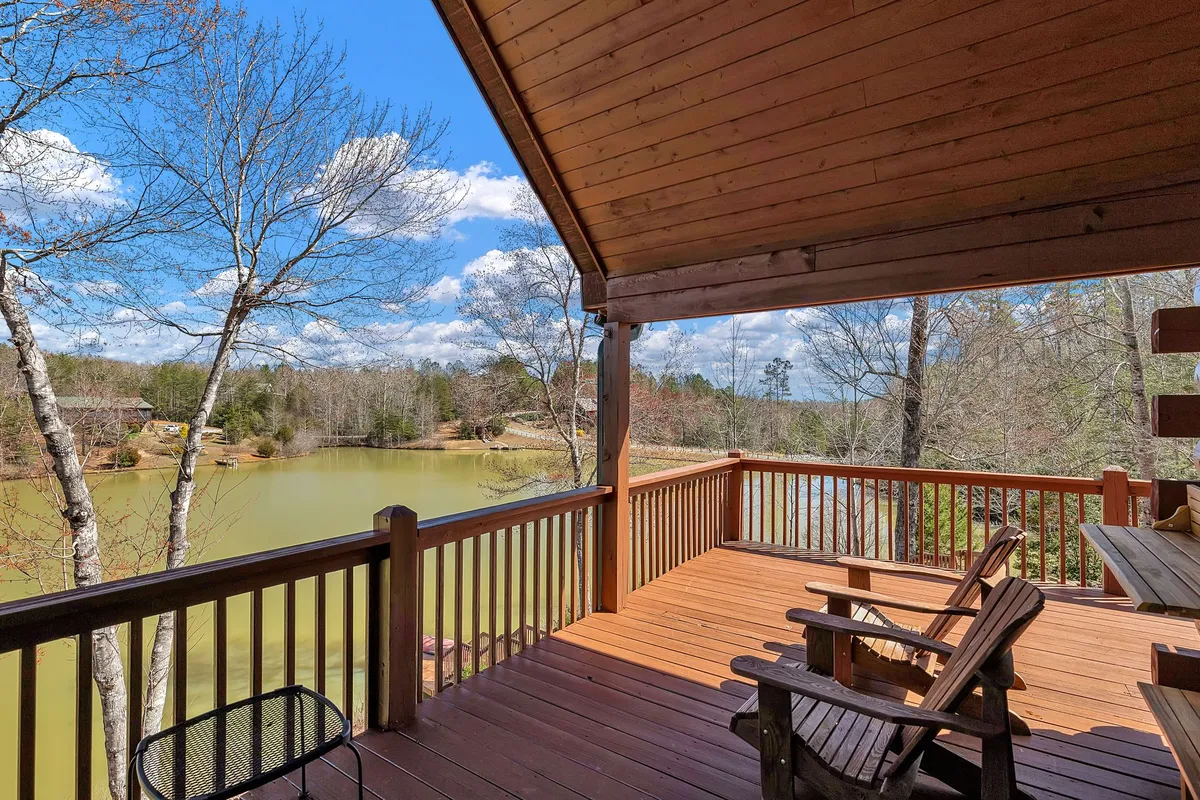 An expansive wooden deck with comfortable outdoor seating, surrounded by trees and overlooking the serene lake. The deck invites guests to relax, socialize, or barbecue while soaking in panoramic water views.