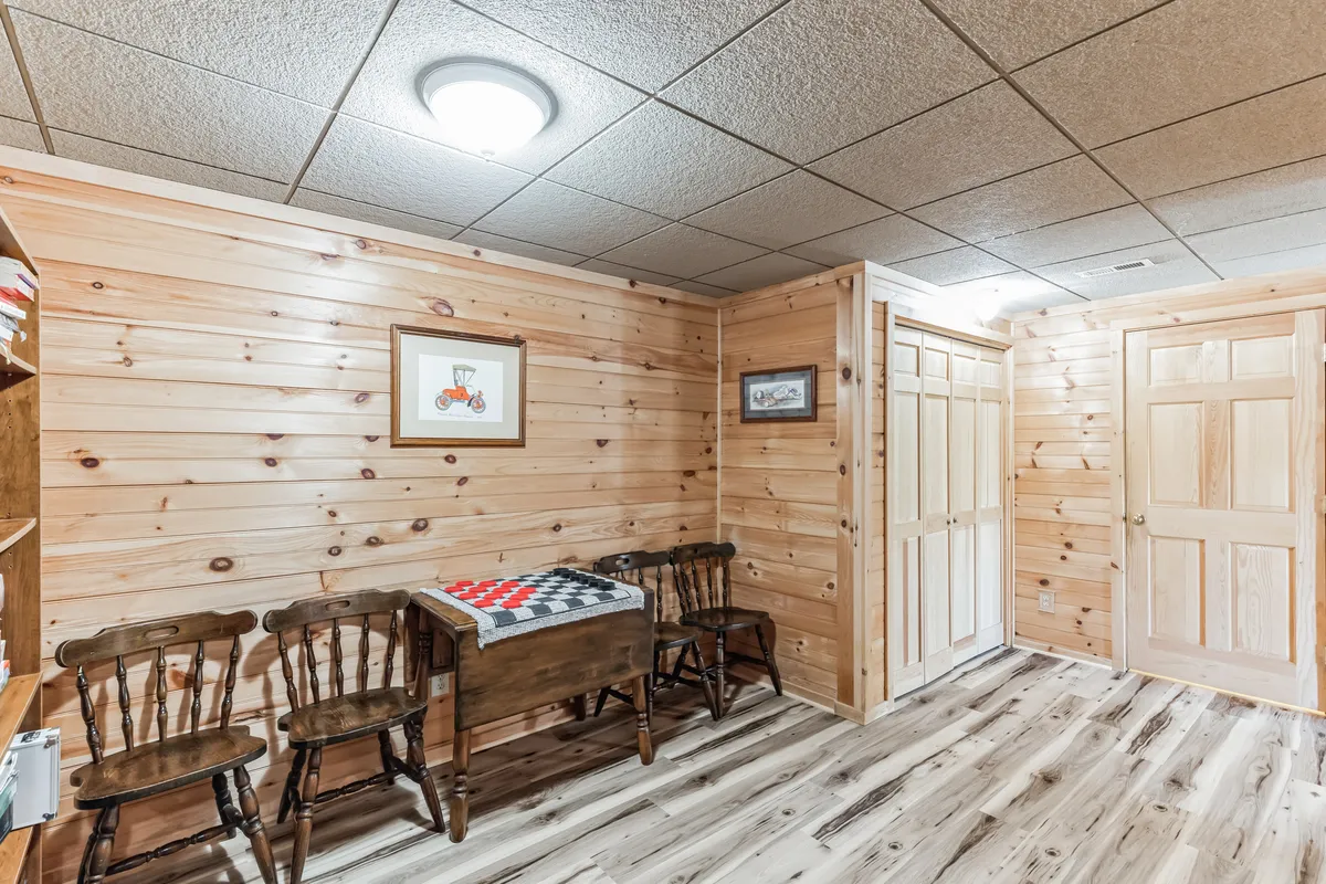 A cozy dining area featuring a wooden table with a checkered cloth surrounded by four wooden chairs. The walls are adorned with framed artwork, creating a welcoming ambiance perfect for group gatherings, board games, or sharing meals.