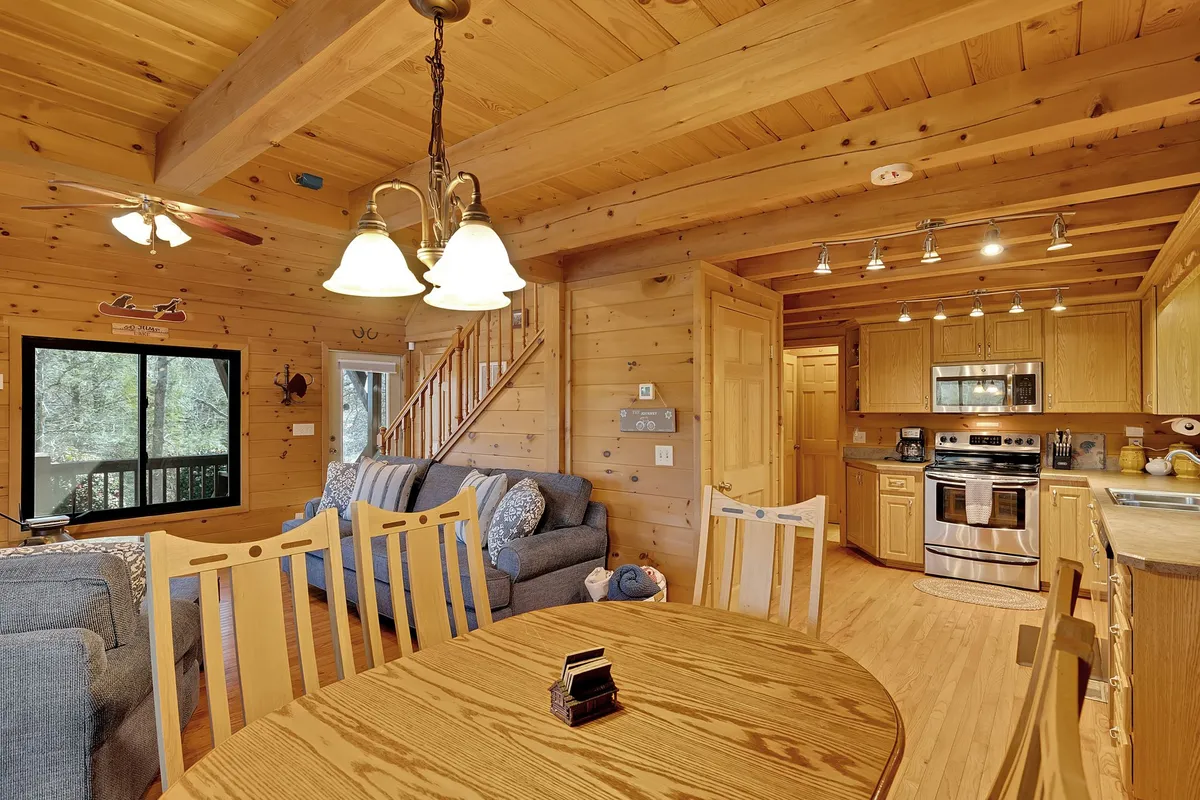 A combined living and dining area featuring a wooden dining table, comfortable sofa, and a modern, fully equipped kitchen with stainless steel appliances. Large windows offer natural light and scenic views, making this space perfect for shared meals, cooking together, or lingering conversations.